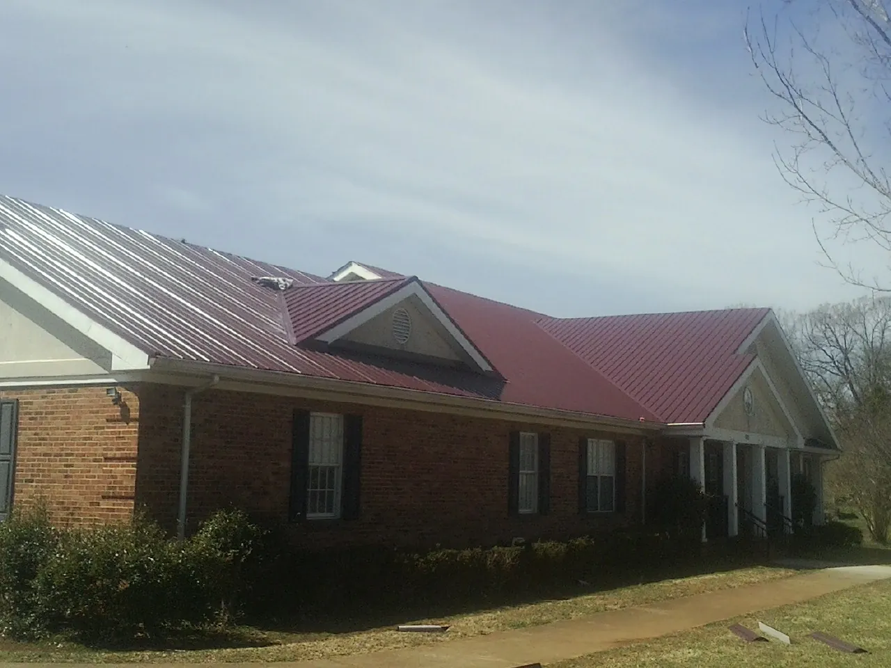 Red metal roof with gabled entries on a long brick building, from a Hail Damage Roof Repair job in Fullerton