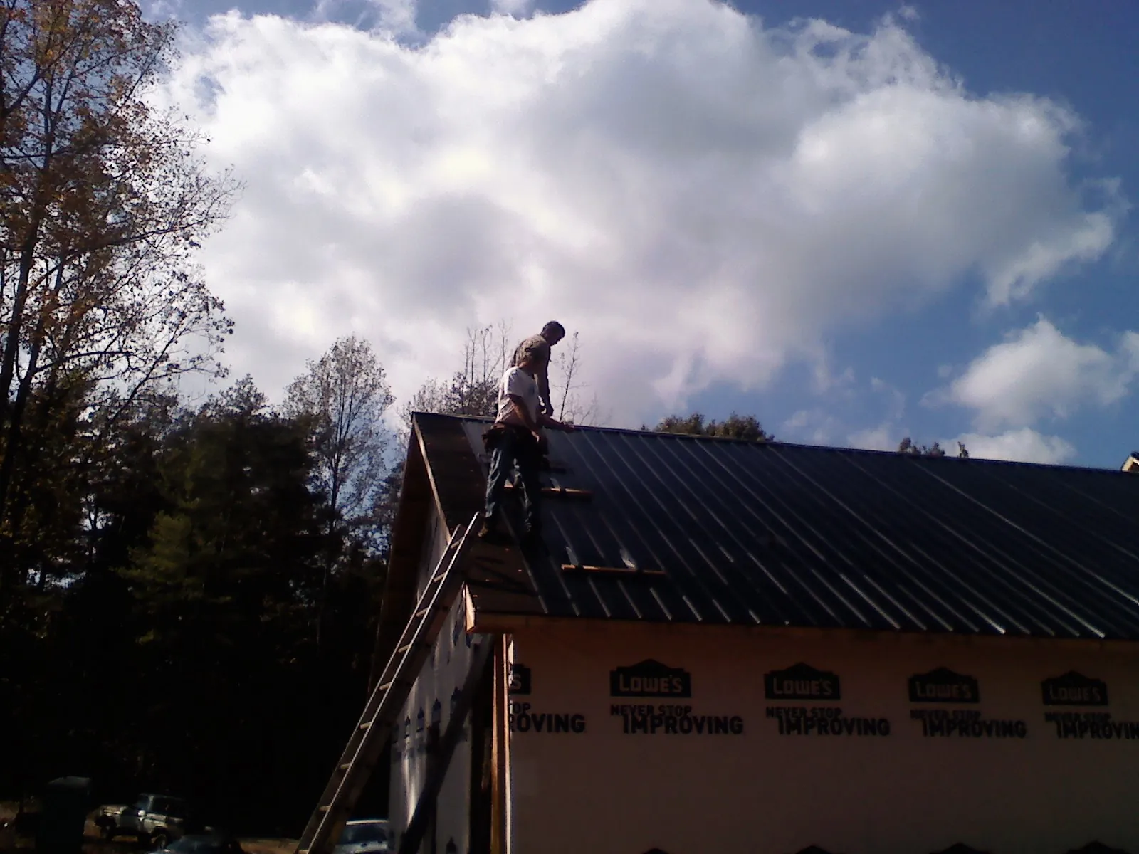 Roofer fastening dark metal panels high against a cloudy sky, from a Roof Inspection job in Fullerton