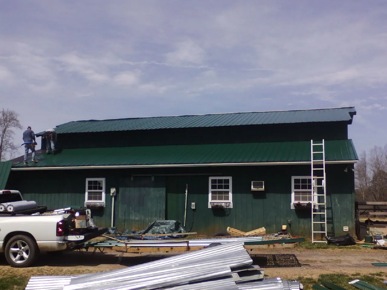 Crew installing green metal roofing on a large green barn in Fullerton