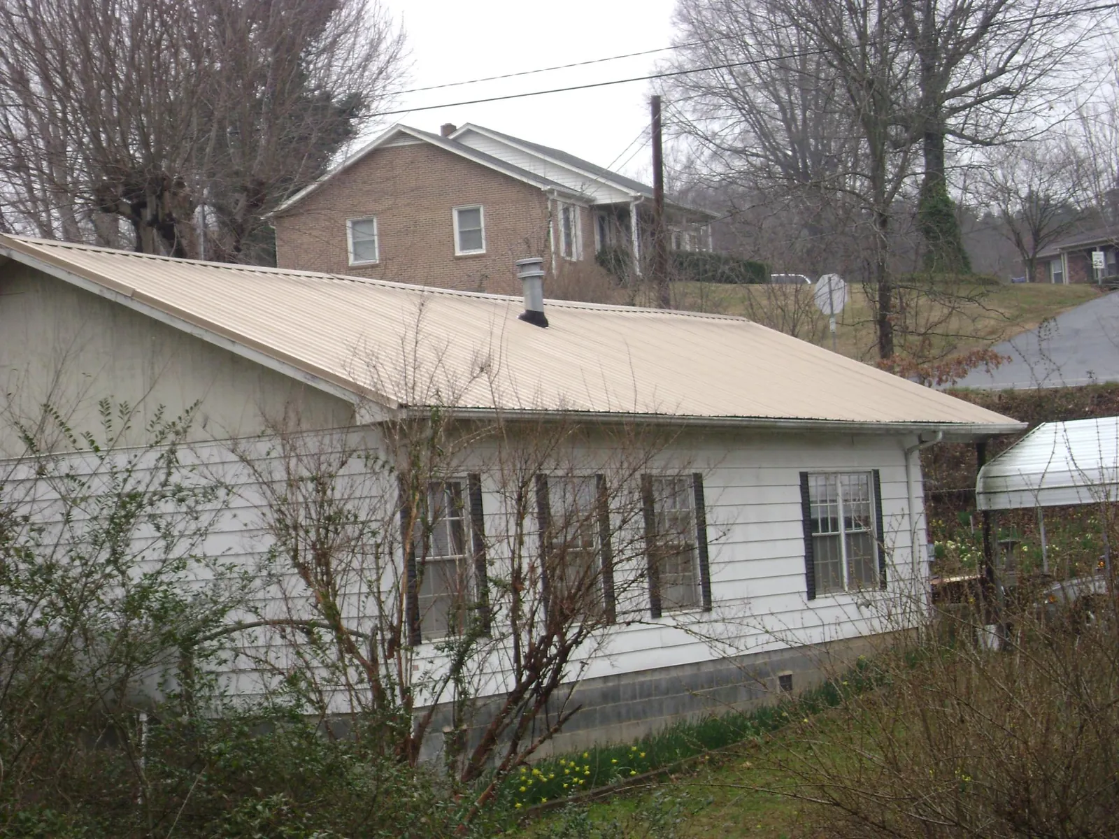 Tan metal roof on a white sided house set into a hillside — Commercial Roofing by Roofing Brothers in Fullerton